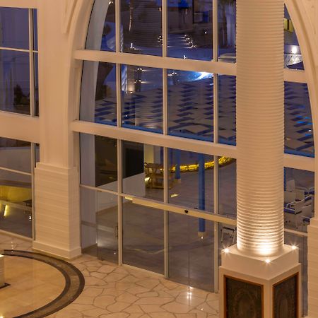 Pickalbatros Palace Sharm - "Aqua Park" Exterior foto The photo shows a spacious interior of a modern building, likely a hotel or a lobby. The scene features large glass windows that allow for a view of areas outside. There are elegant pillars within the space, illuminated from the base, creating a warm