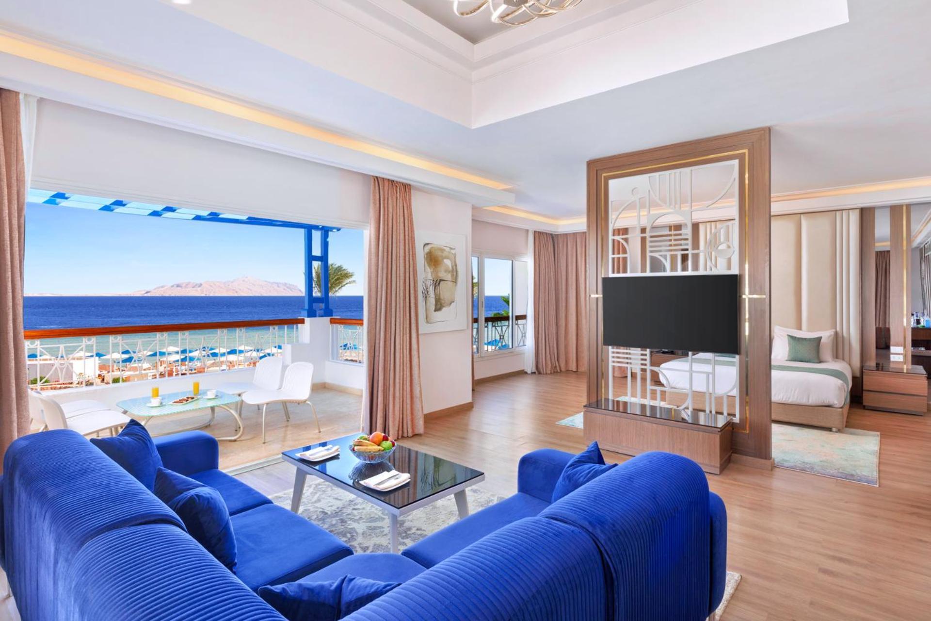 Pickalbatros Palace Sharm - "Aqua Park" Exterior foto The photo shows a well-appointed hotel room or suite featuring a modern and stylish design. There is a spacious living area with a large blue sofa and a glass coffee table in the center. The room is bright, with natural light coming in from large win