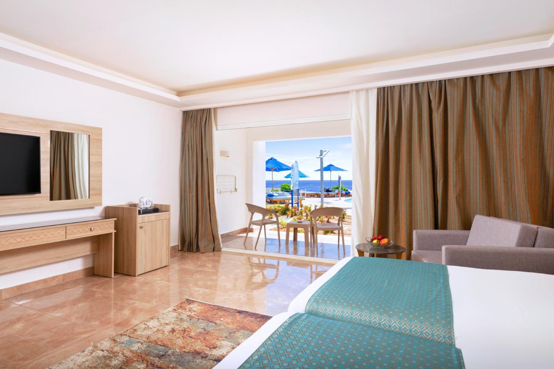 Pickalbatros Palace Sharm - "Aqua Park" Exterior foto The photo shows a spacious hotel room designed with a modern and elegant style. It features two beds with teal-colored bedding, a large mirror, and a television on the wall. There are wooden furniture pieces, including a dresser and a small table. To