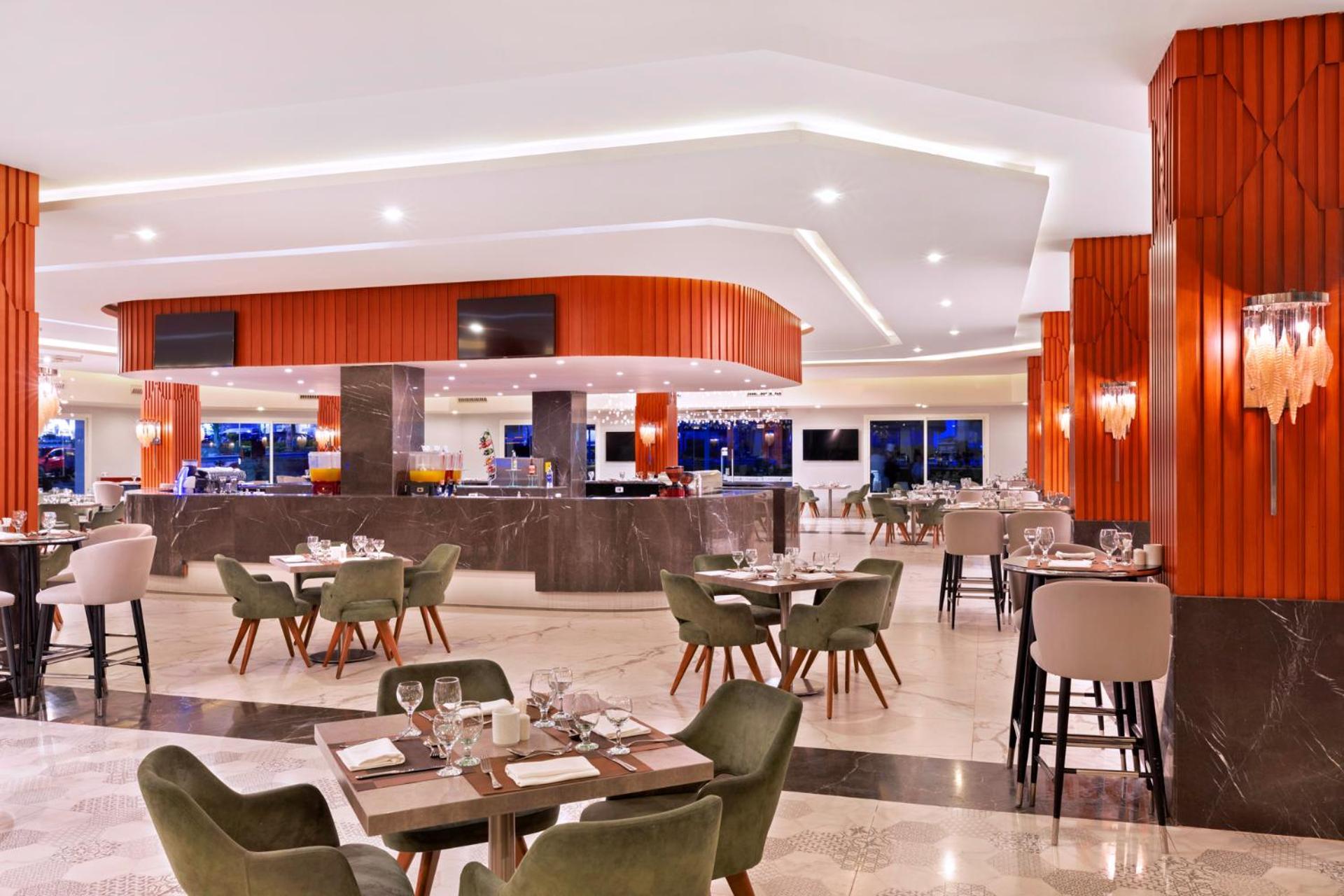 Pickalbatros Palace Sharm - "Aqua Park" Exterior foto The photo depicts a modern restaurant interior. The space features a stylish bar area with a curved counter and bright lighting. There are multiple dining tables set with tableware, including plates and glasses. The design includes a mix of seating o